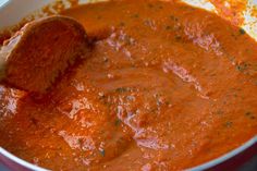 a red pot filled with tomato sauce and a wooden spoon sticking out of the top