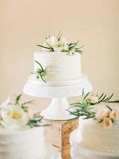 three tiered white wedding cake with flowers on each layer and greenery at the top