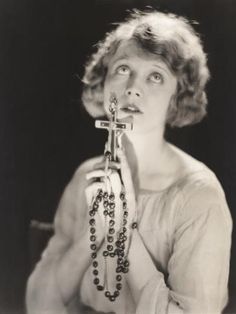 an old black and white photo of a woman holding a cross in her hands with beads around her neck