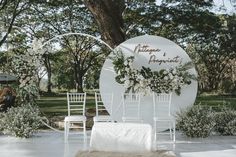 an outdoor wedding setup with white chairs and greenery on the back drop off table