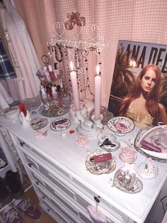 a white dresser topped with lots of pink and silver items next to a poster on the wall