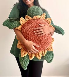 a woman holding a crocheted sunflower pillow in her arms and smiling at the camera