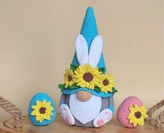 a crocheted bunny with sunflowers on it's head sitting next to three eggs