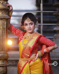 a woman in a yellow and red sari standing next to a lamp post with her hands on her hips