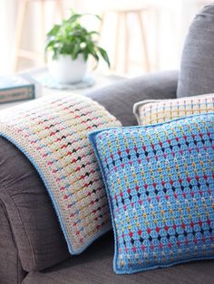 two crocheted pillows sitting on top of a couch next to a potted plant