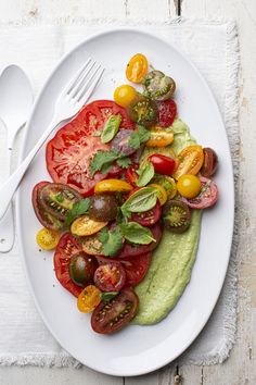 a white plate topped with sliced tomatoes and avocado