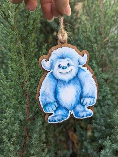 a hand is holding a blue ornament with a smiling yeti on it