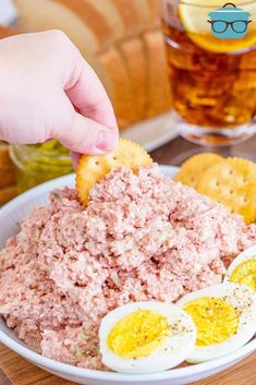 a person dipping an egg into a bowl of tuna salad with crackers on the side