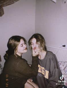 two young women sitting next to each other on a bed with their faces painted white