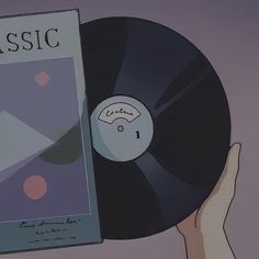 a hand holding an old record in front of a book with the word classic on it