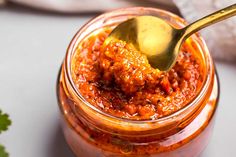 a spoon in a jar filled with chili sauce and garnished with parsley