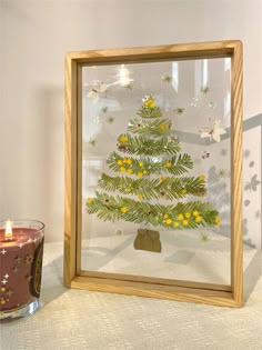 a lit christmas tree in a frame next to a candle