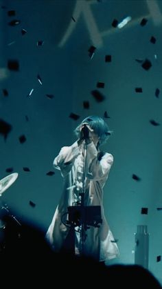 a man standing on top of a stage next to a drum set and microphone in front of him