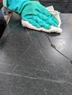 a person in blue gloves and green mitts cleaning a black counter with a rag