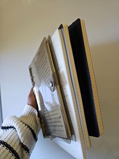 a person holding an open binder with notes attached to it, in front of a white wall