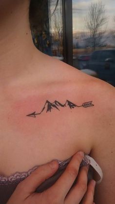 a woman's shoulder with an arrow and mountains tattoo on her left side chest