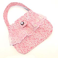 This is a darling little girl's pink and white purse made from a 100% cotton fabric featuring a swirling white leaf pattern on a pink background.  The lining is 100% cotton in a white-on-white print fabric.  The purse is finished with a shimmery pink lace trim along the front and back, and a sparkly pink faceted rhinestone button for the closure. There is a small inside pocket as well. Are you looking for the perfect gift for the special little girl in your life?  If yes, then this may be what you are looking for!   Approximately 7" wide Approximately 5 1/2" tall, plus 3 1/2 inches for the handle. Approximately 9" tall overall. I designed this purse and made my own pattern. This purse would make the perfect little handbag gift for Christmas, Easter, or birthday.   Not intended for children White Purse, Girls Purse, White Purses, White Leaf, Gift For Christmas, Pink Lace, Pink Background, Print Fabric, Leaf Pattern