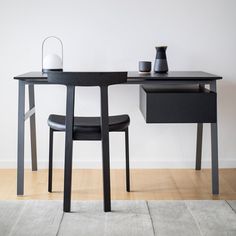 a black desk and chair in front of a white wall with a vase on it