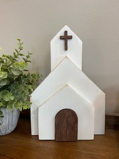 a small white church with a cross on the top and a potted plant next to it