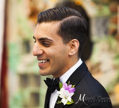 a man in a tuxedo smiles at the camera while wearing a flower on his lapel