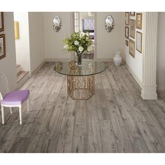 a glass table with flowers on it in the middle of a room that has white walls and wood flooring