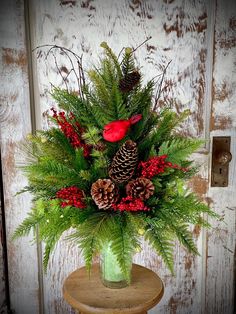 a green vase filled with pine cones and red berries on top of a wooden table