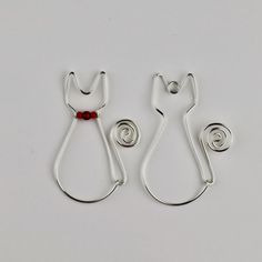 two silver cat shaped brooches with a red bead on each earring