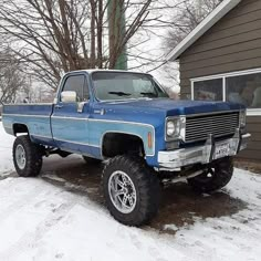 a blue pickup truck parked in front of a house with snow on the ground and trees