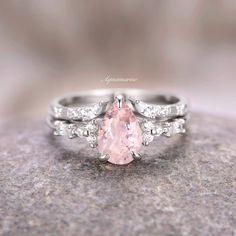 a pink diamond ring sitting on top of a gray rock with diamonds around the band