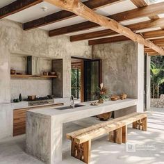 an outdoor kitchen with concrete counter tops and wood beams on the ceiling, along with wooden benches