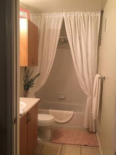 a bathroom with a toilet, sink and bathtub covered in white curtained drapes