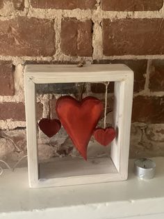 two red hearts are hanging in a white frame on a shelf next to a brick wall