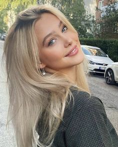 a woman with long blonde hair standing in front of a street and looking at the camera