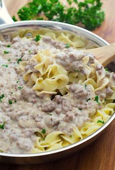 a pan filled with pasta and meat sauce on top of a wooden table next to parsley