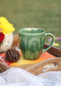 a green coffee cup sitting on top of a wooden tray next to a flower arrangement