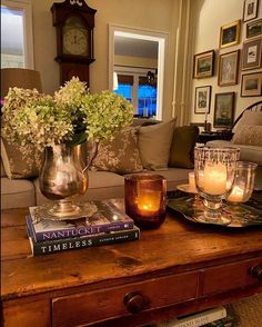 a coffee table with candles and flowers on it in front of a couch next to a clock