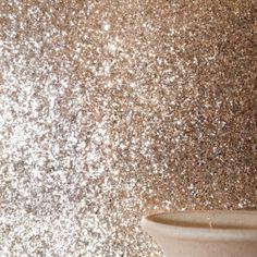 a white vase sitting on top of a table next to a wall covered in glitter