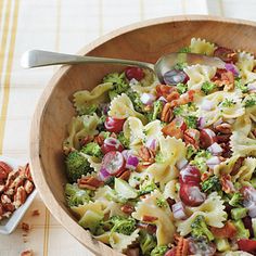 a wooden bowl filled with pasta salad next to two bowls of nuts and other food