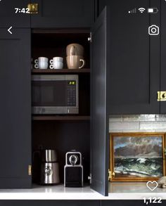 a kitchen with black cabinets and white counter tops is shown in this image, there are coffee mugs on the shelves