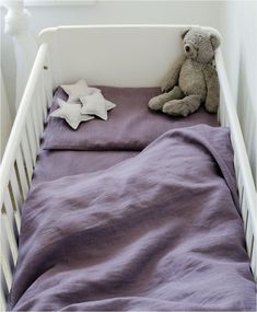 a teddy bear sitting on top of a purple blanket in a white crib next to pillows