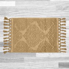 a beige rug with fringes on top of a wooden floor next to a white wall