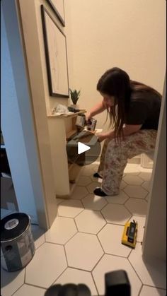 a woman kneeling down on the floor in front of a sink with tools around her