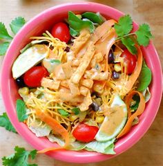 a pink bowl filled with salad and dressing on top of a wooden table next to tomatoes