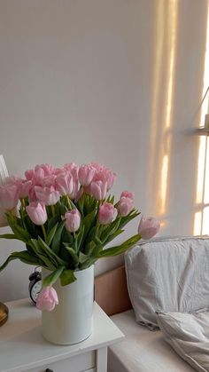 a white vase filled with pink tulips sitting on top of a small table