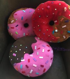 three donuts with sprinkles are sitting on a black surface, one is pink and the other is chocolate