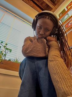 a young woman wearing headphones sitting in front of a window with her hand on her chin