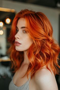 Woman with wavy red hair and light skin in a grey top, looking off to the side in a dimly lit room. Highlights In Short Brown Hair, Latest Hair Color Trends