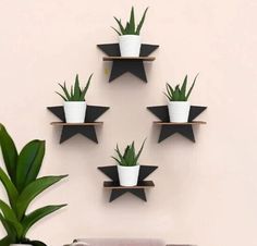 four black and white star shaped wall shelves with plants on them, against a pink wall