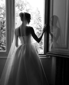 a woman standing in front of a window wearing a wedding dress and holding her veil