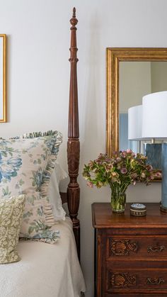 a bedroom with a bed, mirror and flowers on the nightstands in front of it